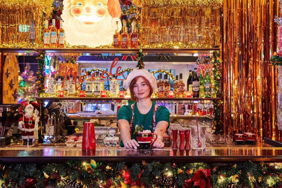 This is a picture of the Miracle Christmas-themed cocktail bar at Henrietta Hotel where the whole bar is lit up with decorations and the bartender is in an elf costume.