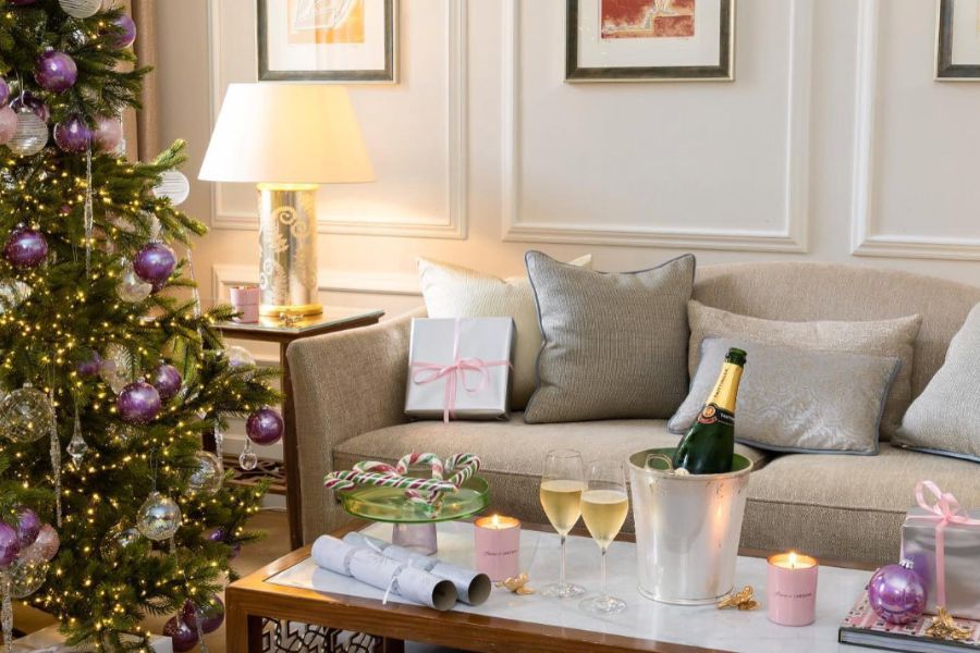 This is a picture of The Langham's hotel rooms at Christmas time. There is a lit-up tree in the left corner and the coffee table is full of champagne, baubles and Christmas crackers.