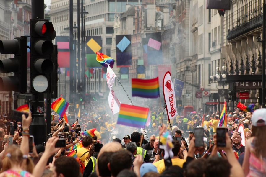 Crowds lining the streets of central London during Pride parade, with rainbow flags waving above a sea of people on a busy city street.