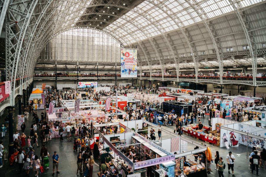 Aerial view of the Hyper Japan Festival at Olympia London, with hundreds of visitors browsing colourful stalls beneath the venue's grand arched glass roof.