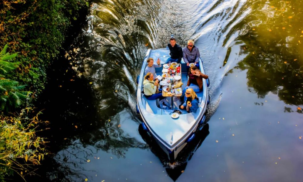 This is an image of people riding a GoBoat through the canals of London with a table full of picnic goodies.