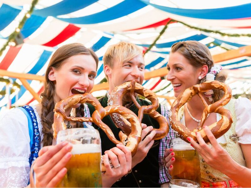This is an image of three people eating pretzels and holding big pints of beer for Oktoberfest.