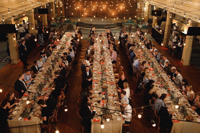 A grand ballroom for the Marylebone Food Festival in April with three long tables and 100 people seated eating high end food.