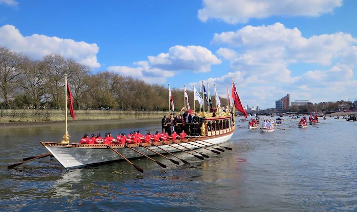 The Boat Race happening on the River Thames, with a large boat at the front and many small ones behind. One of the top things to do in April in London.