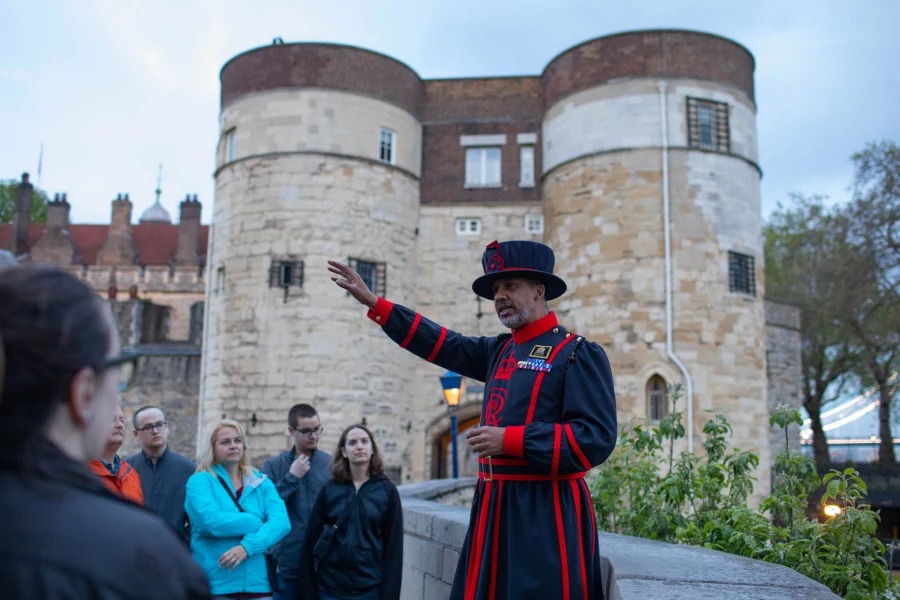 This is an image of a man in uniform giving a tour to a group of people stood in front of a historical building.