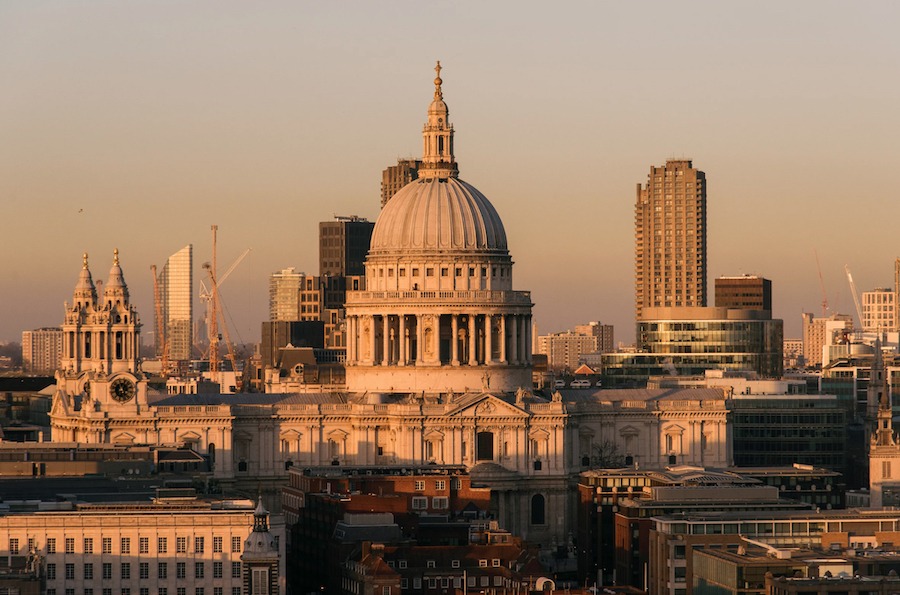 This is an image of a dome shaped cathedral in a busy city with a pretty skyline. It is dusk and the sun is about to set.