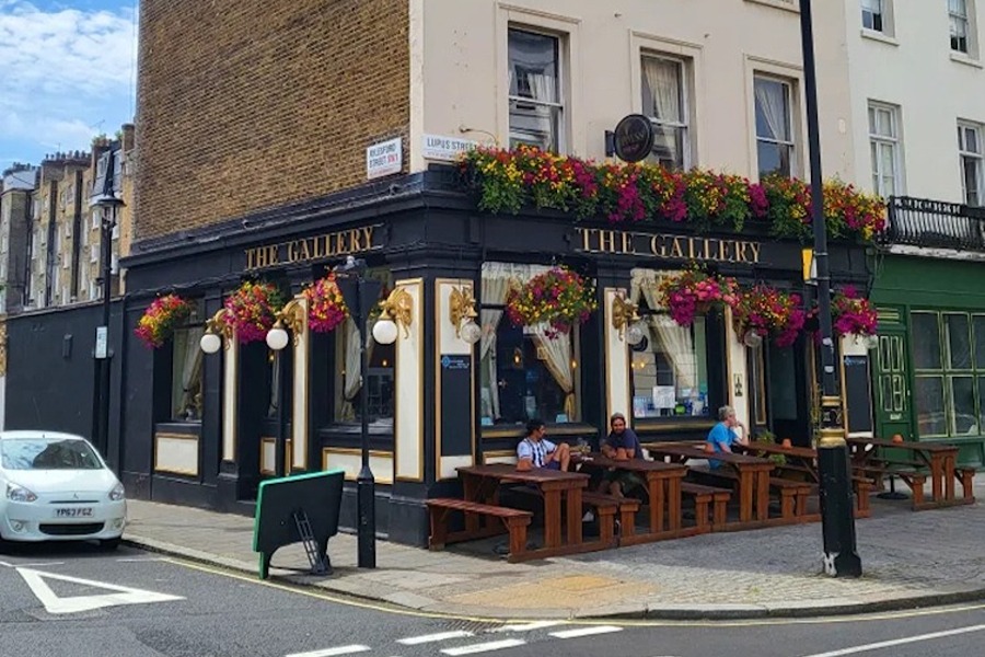 Picture of the exterior of The Gallery, one of the best London hostels, with brick walls and white facade. There’s a pub on the ground floor with flowers all around.