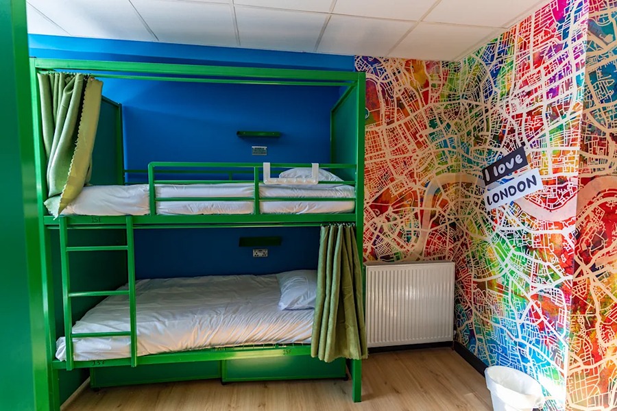 Two green bunks in the middle of a brightly coloured hostel room in London.