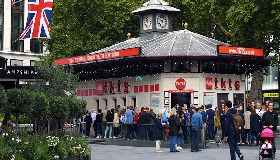 This is a picture of the TKTS box office in Central London. There is a small crowd milling out the front. One of the things to know before booking London theatre tickets is that you can get limited same-day discounted tickets if you go to the box office early on the day you want to go.