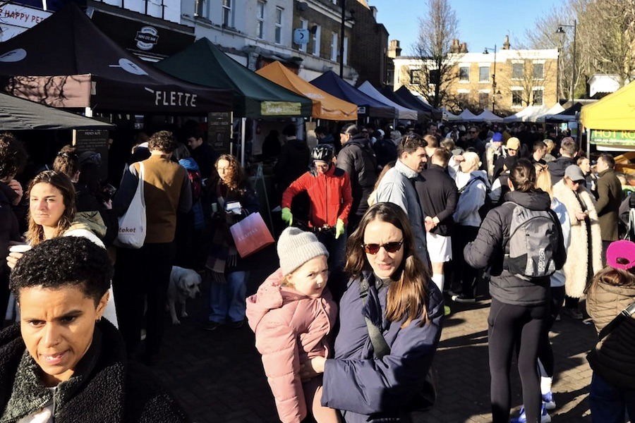 This is an image of a big market street filled with people walking through and small food stalls.