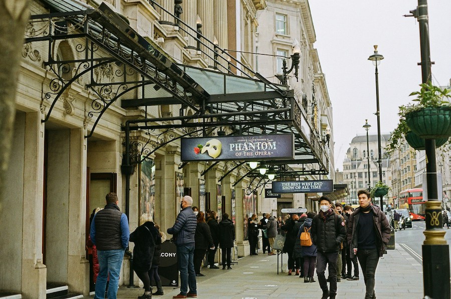 This is an image of the street in front of the theatre showing The Phantom of the Opera. People are milling around in smart-casual, comfortable clothes waiting to get in. One of the things to know before booking London theatre tickets is that you don't need to adhere to a specific dress code.