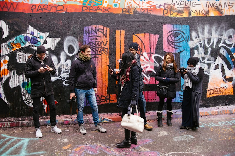 This is an image of a graffitied wall in Brick Lane London. Several people are standing in front of the art. It is said that staying in very touristy areas is a mistake people make when planning their London itinerary. Brick Lane is a good spot off-the-beaten-path