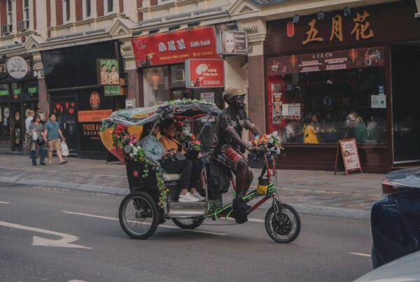 This is an image of a man riding a rickshaw with two women in the back laughing.