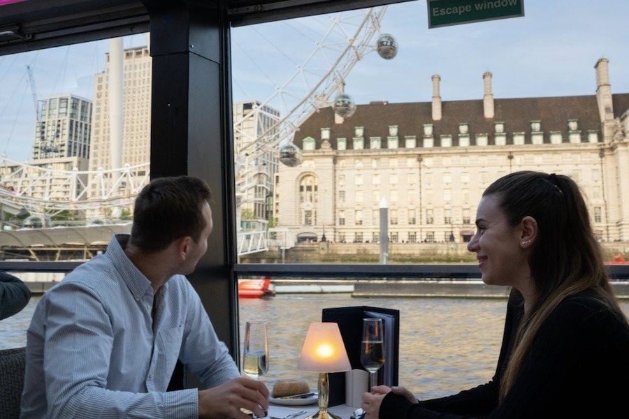 This is an image of two people having dinner together with a romantic candlelight in front of them and picturesque views of the London Eye.