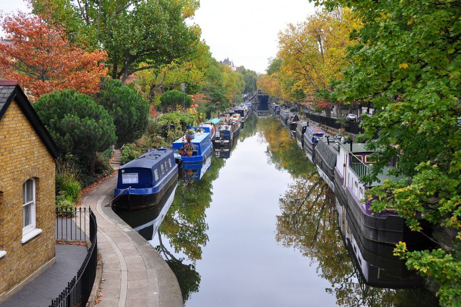 This is an image of a canal lined with barge boats and autumnal trees.