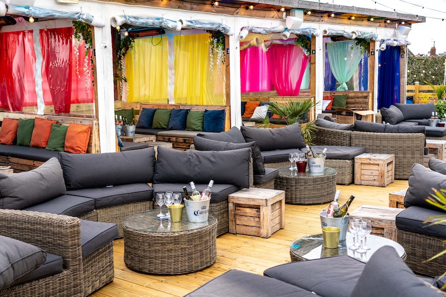 This is an image of a rooftop bar with colourful decorations and lots of lounge chairs on the patio.