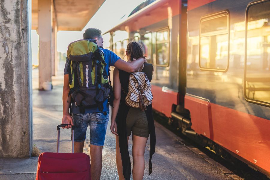 This is an image of two travellers carrying their backpacks and suitcases down a train platform