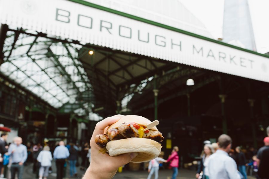 Why people might not enjoy their trip to London: they don't budget and spend loads. This is an image of someone holding up a burger in front of the Borough Market entrance. This is a place people come to eat street food for cheap.