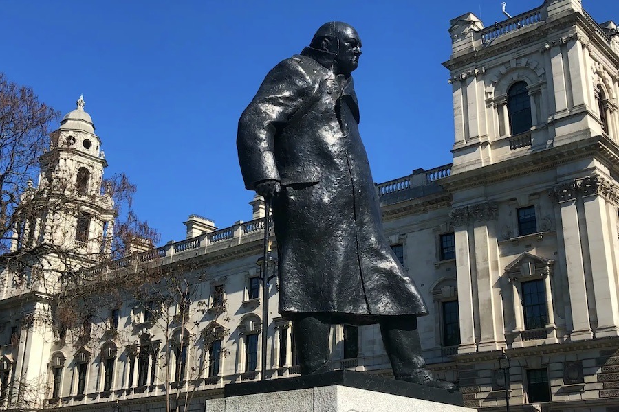 This is an image of the Winston Churchill statue with buildings and a blue sky behind it.
