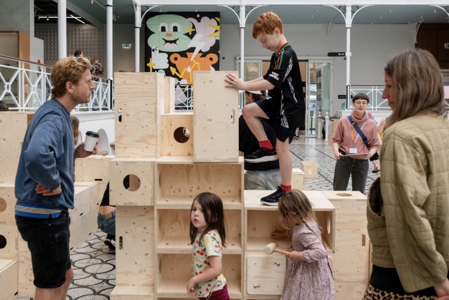 This is an image of a bunch of kids playing on a wooden block with their parents watching on